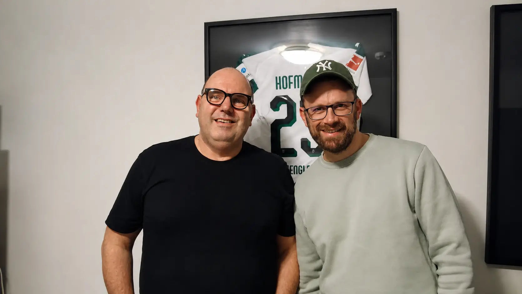 Felix von trikotrahmen.de und Trikot-Experte Stefan Appenowitz vor einem gerahmten Trikot bei der Aufnahme des Stoffkunde Podcasts