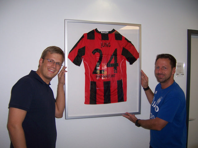 Uwe Bindewald im NLZ von Eintracht Frankfurt vor dem gerahmten Trikot von Sebastian Jung