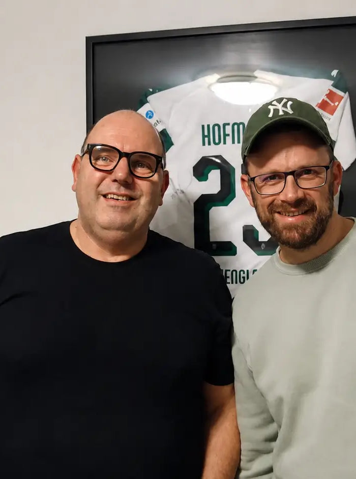Felix von trikotrahmen.de und Trikot-Experte Stefan Appenowitz vor einem gerahmten Trikot bei der Aufnahme des Stoffkunde Podcasts